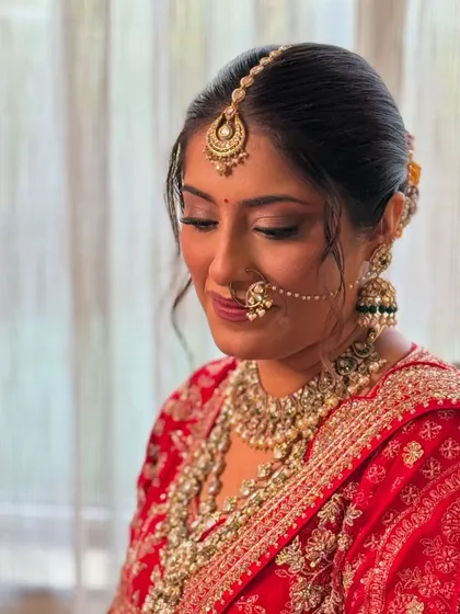 A classic bridal look featuring soft smokey eyes and a mauve lip color, paired with a traditional red lehenga and heavy Kundan jewelry.