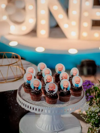 Themed cupcakes for a "Boss Baby" first birthday. Each cupcake is topped with an edible image of the Boss Baby, placed in front of the glowing 'ONE' marquee lights.