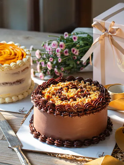 A duo of our signature mini cakes perfect for a weekend celebration. On the left is our Vanilla & Mango cake with a mango rose topping, and on the right is our Dark Chocolate & Salted Caramel cake with a crunchy praline topping.