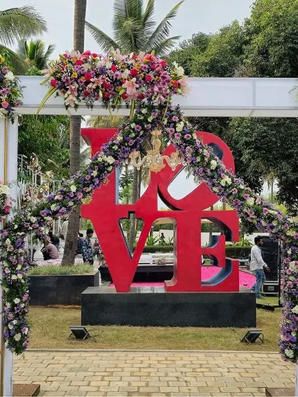 A modern and romantic entrance featuring white arches adorned with flowers, perfectly framing a large red "LOVE" sculpture. It's a perfect photo opportunity for guests.