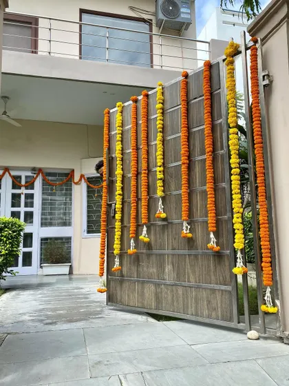 A simple and traditional way to welcome guests during any festival is with fresh flower garlands on the main gate. Here, I have used long strings of orange and yellow genda (marigold) flowers.