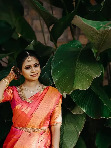A lovely portrait of a South Indian bride, her traditional attire and jewelry shining against a lush green background.