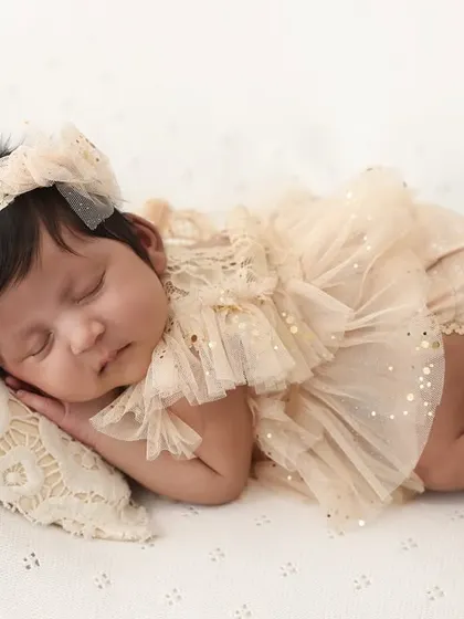 Capturing the peaceful slumber of a newborn baby. This side-profile shot beautifully details the baby's tiny features while she sleeps in her adorable ruffled outfit.