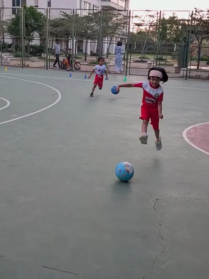 A young girl leaps in the air, full of joy and energy during a football session on an outdoor court.