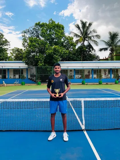A solo shot of Manish with his singles trophy against a beautiful outdoor court backdrop.