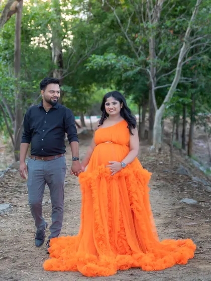 A happy couple enjoying a walk together on a path in the woods. The mom-to-be's orange gown brings so much brightness to this natural, candid-style shot.