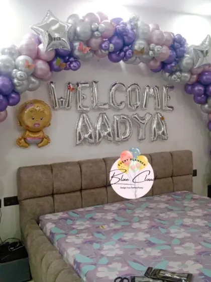 A 'Welcome Aadya' bedroom decoration with a purple and silver balloon arch over the bed.