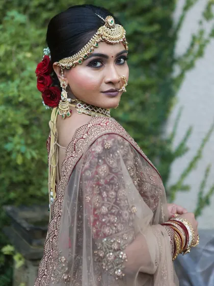 A beautiful side profile showing the elegant bridal bun adorned with red roses and the flawless makeup.