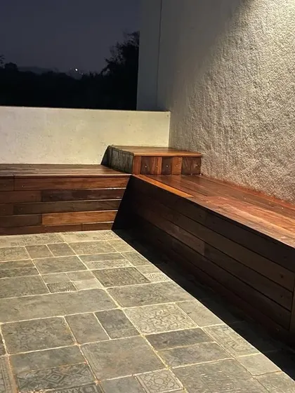 We design and build custom outdoor furniture and seating, like this integrated wooden bench on a stone-paved patio, providing a permanent and stylish resting spot.