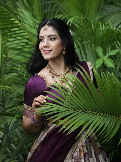 A creative portrait where the model is framed by a large palm leaf, adding a natural and artistic element to the traditional attire.