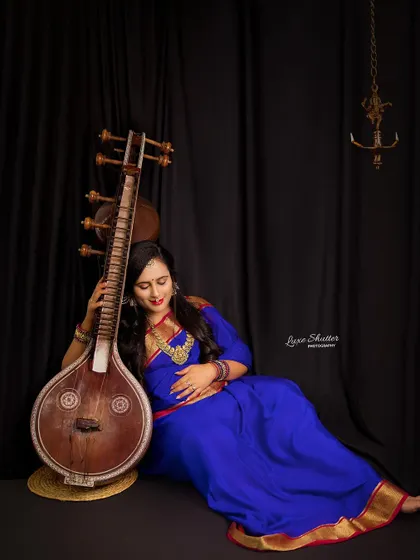 A relaxed and graceful pose, where the mother-to-be rests against her Veena. The dark background and simple lighting create an intimate and soulful mood.