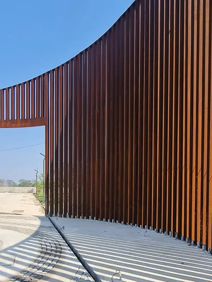 The curved Corten steel gate creates a sense of enclosure while remaining visually permeable, offering glimpses of the landscape within.