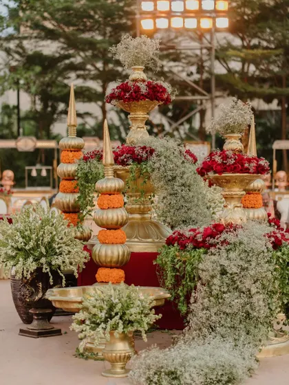 A beautiful centerpiece for a traditional ceremony, featuring stacked golden vessels, marigold flowers, and cascading baby's breath.