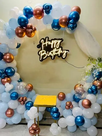 A stylish birthday balloon ring in shades of blue, white, and copper, with a "Happy Birthday" neon sign.