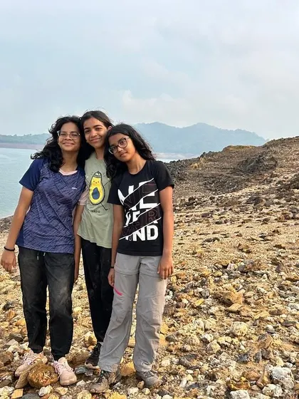 Three friends pose for a photo on the rocky shore, memories made during their adventure camp.