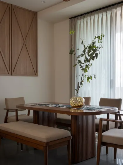 A wider view of the dining space, showing its connection to the living area. Daylight filters in through sheer curtains, creating a bright and open atmosphere for shared meals.