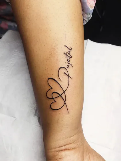 A name tattoo, 'Pujatul', integrated with two intertwined hearts. This design beautifully combines a name with a symbol of love.