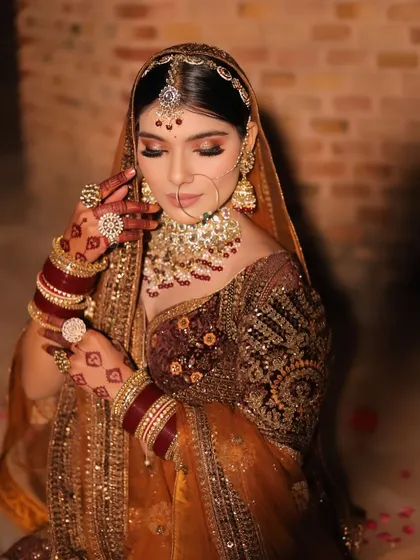 A delicate and graceful portrait of the bride. Her eyes are closed and her hands gently frame her face, drawing attention to her intricate rings and henna design.