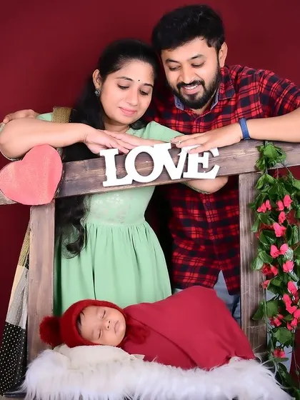 A loving family portrait with parents admiring their newborn baby in a "love" themed setup.