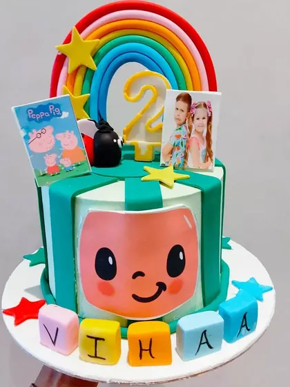 A colorful Cocomelon themed cake for a 2nd birthday. The design incorporates elements from the show, along with photos of the birthday twins.