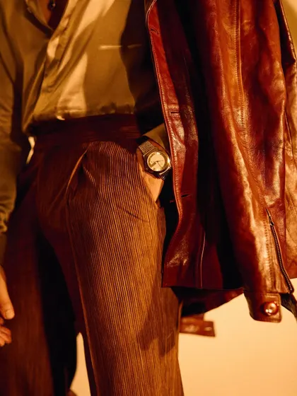 A detail shot focusing on the pleated trousers and the luxury watch, showcasing how every element, from the main garments to the accessories, is carefully considered.