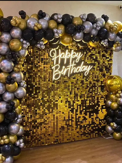 A luxurious black and gold theme featuring a gold shimmer wall. The wall is framed by an L-shaped balloon arch and lit by a "Happy Birthday" neon sign.