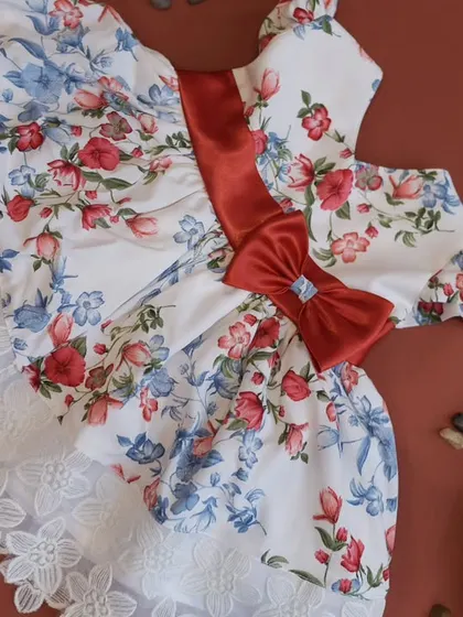 Another angle of the white floral dress with the red sash, showing the delicate white lace trim at the hem for an extra touch of elegance.