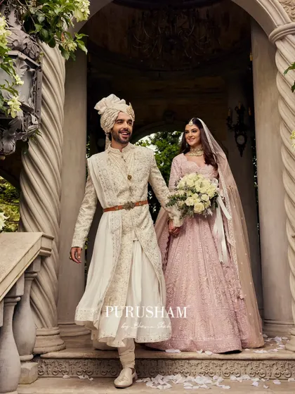 A joyful moment from a wedding, showcasing the groom's custom-fit sherwani. The intricate white-on-white embroidery and the elegant drape of the fabric are designed to look impeccable from every angle.