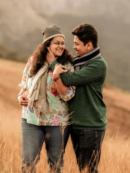 An intimate and cozy pre-wedding portrait of a couple in warm winter clothing, sharing a hug in a field of dry grass.