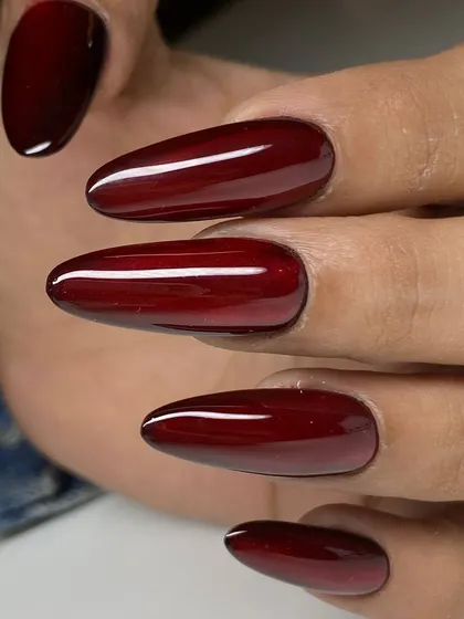 A stunning deep crimson polish on long, almond-shaped nails. The rich, glossy color is dramatic and elegant.