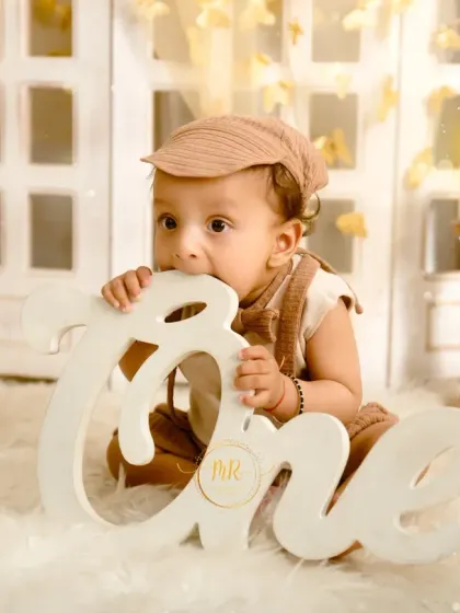 A baby boy celebrating his first birthday with a boho-themed shoot, chewing on a large "One" sign.