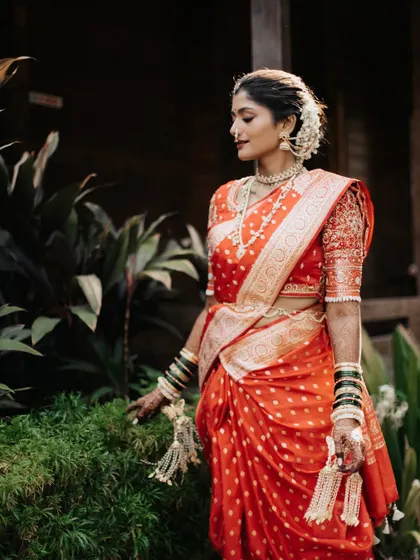 A graceful portrait of the bride in her vibrant orange saree, surrounded by lush greenery.