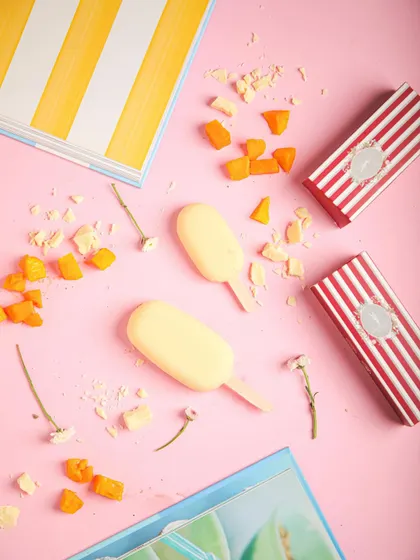 Our mango ice cream bars, a sweet and fruity frozen fix, surrounded by pieces of fresh mango.