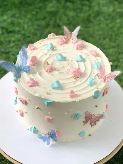 A white cake with a swirl top, decorated with blue and pink hearts and edible butterflies.