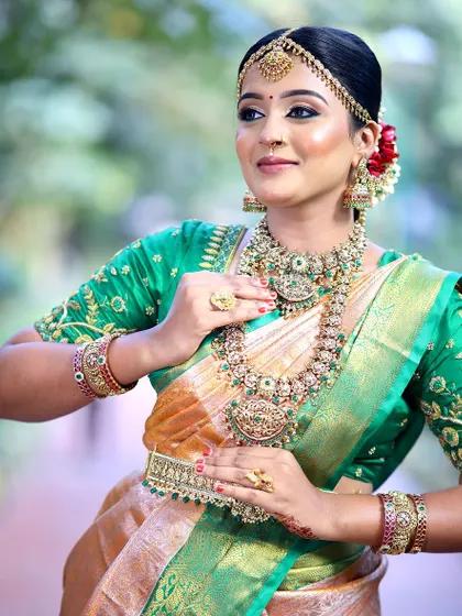 A beautiful bride in a green and orange Kanjeevaram saree. We designed the blouse with detailed Maggam work to match the richness of the silk, creating a perfect bridal ensemble.