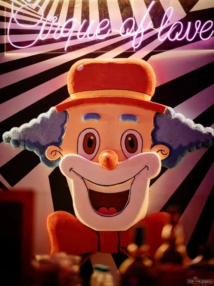 A quirky, oversized clown face with a 'Cirque of Love' neon sign above it, serving as a bold and playful decor piece for the circus-themed after-party bar.