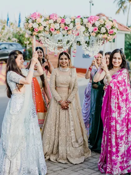 The bride's grand entrance under a floral canopy. Her golden look is absolutely breathtaking, making her the center of attention.