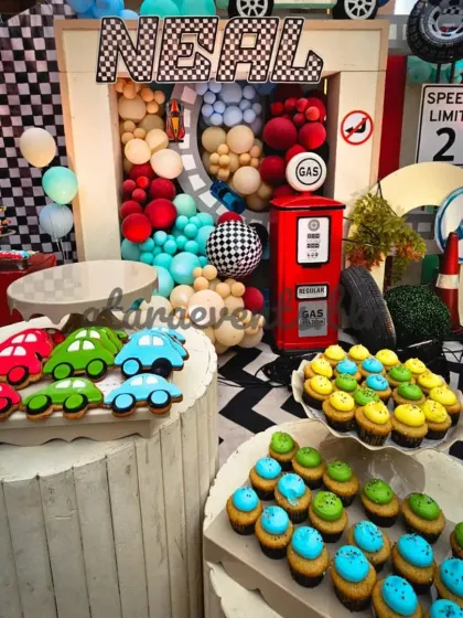 The dessert table is a pit stop for delicious treats, featuring car-shaped cookies and themed cupcakes set against the dynamic backdrop of the main stage.