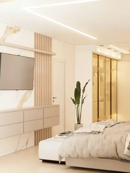 A bright and luxurious bedroom with a marble and wood-panelled TV wall, and a walk-in closet with gold-tinted glass doors.