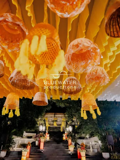 A creative ceiling installation for a Haldi, featuring yellow drapes and an assortment of hanging wicker and tassel lampshades.
