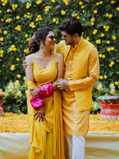 A stylish couple poses against a wall of yellow flowers at their Haldi ceremony in Kanpur, a perfect blend of tradition and modern flair.