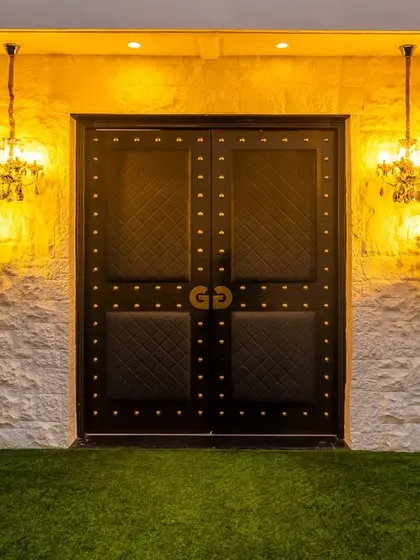 The entrance to the Gallops banquet hall sets the stage for the elegance within. The grand, studded black doors are flanked by classic chandeliers against a textured white stone wall. This design creates a dramatic and welcoming entry, promising a memorable experience for every guest.