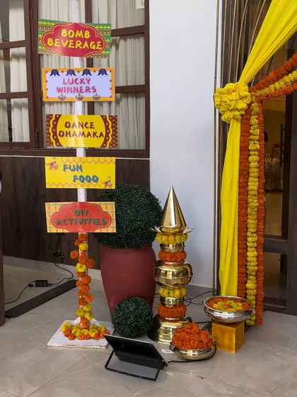 A fun and festive entrance for a Diwali party. The signpost directs guests to "Dance Dhamaka" and "Fun Food," and the area is decorated with marigold garlands and traditional brass elements.
