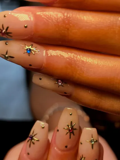 A macro shot of the celestial-themed nail art, detailing the tiny, colorful rhinestones placed in the center of the metallic stars.
