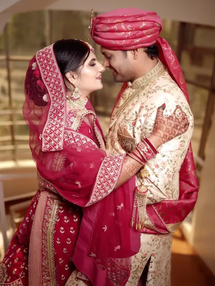 An intimate embrace on the stairs. This close-up shot focuses on the couple's loving expressions and the rich details of their red and cream wedding outfits.