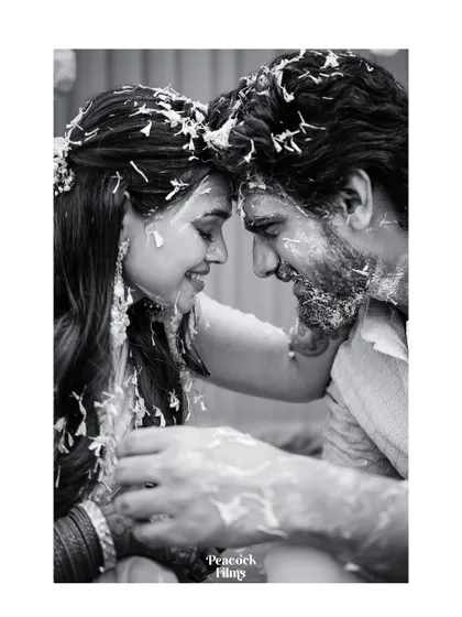 A tender black and white portrait from a Haldi ceremony. The couple, covered in turmeric and petals, share an intimate moment, their foreheads touching.