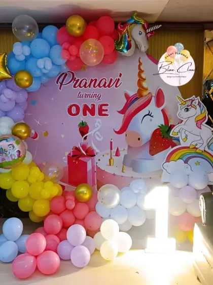 A vibrant unicorn-themed first birthday with a custom backdrop and a multi-colored balloon garland.
