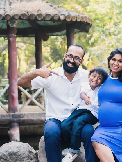 A fun and playful family maternity photo. The whole family is pointing to the baby bump, sharing in the excitement of the new arrival in a beautiful park setting.