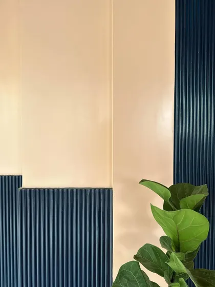 A close-up of the wall treatment, showing the contrast between the smooth peach-colored upper wall and the textured, deep blue fluted paneling below. This detail adds a layer of color and texture to the showroom interior.