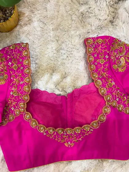 The back of the pink blouse, featuring a deep U-neckline bordered with the same intricate gold embroidery.